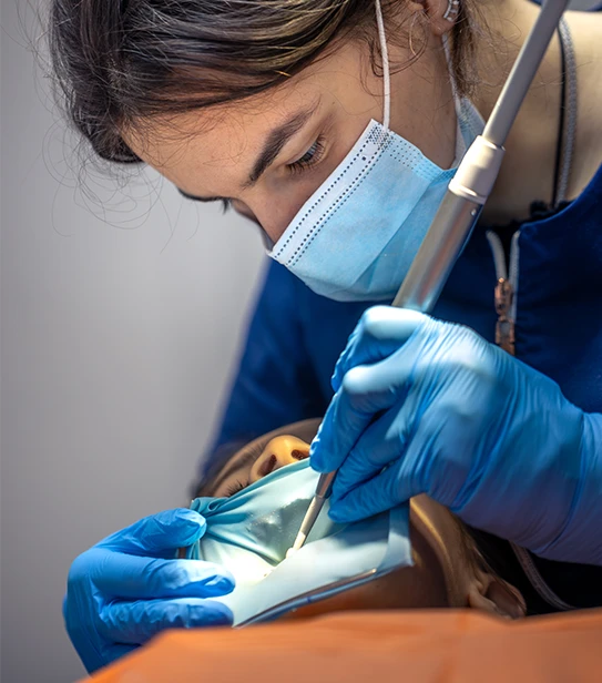 A female dentist performing a precise dental procedure on a child using a light-blue rubber dam to isolate the tooth and maintain a sterile field.