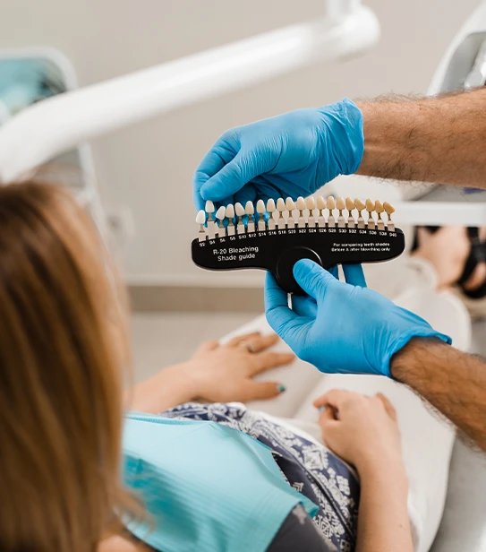 Dentist showing teeth whitening shade guide to patient in dental chair during bleaching consultation