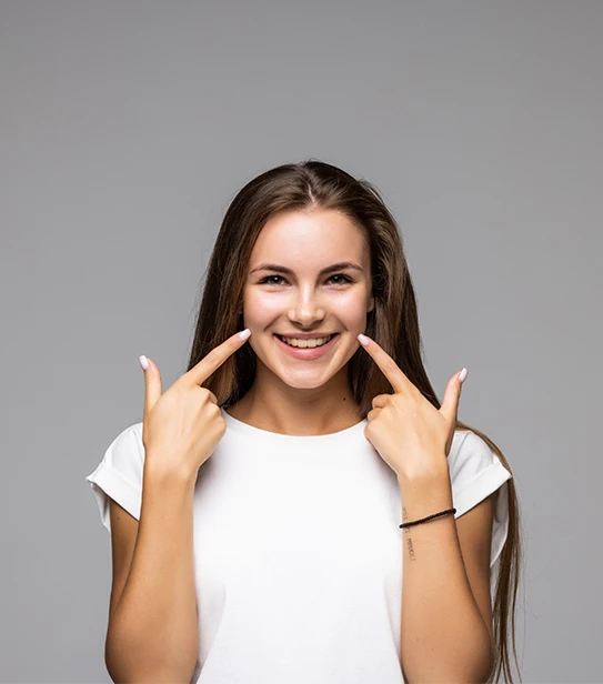 Young woman smiling and pointing to her white teeth against a grey background" — descriptive, natural, and keyword-rich without stuffing